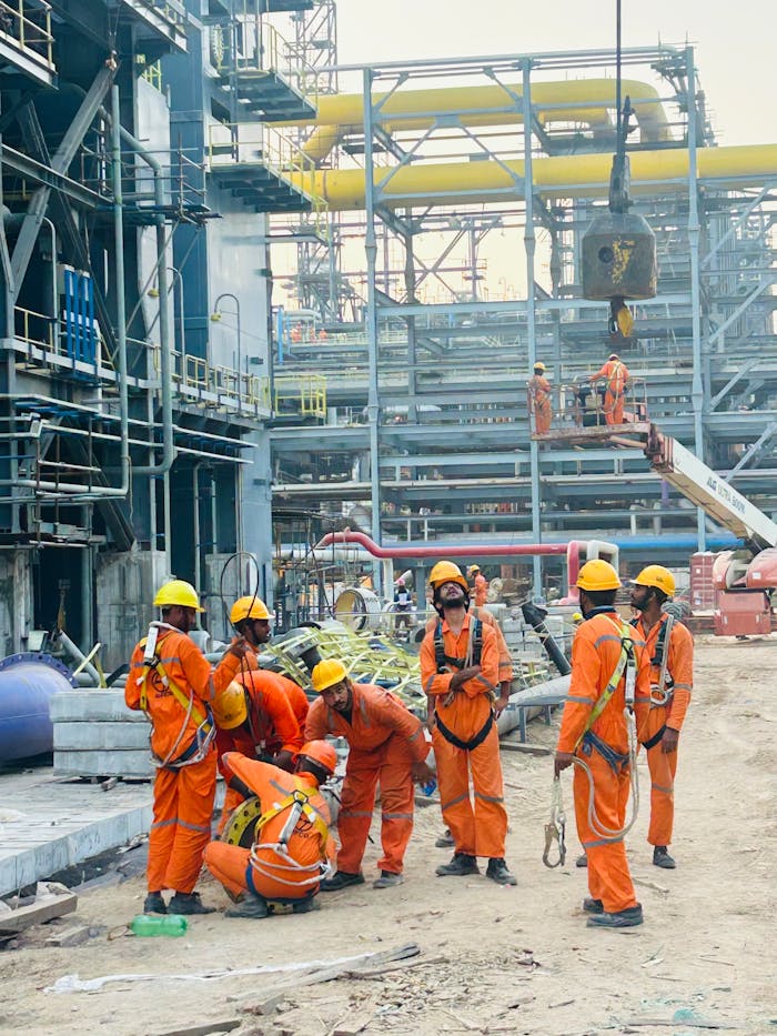 Group of construction workers in orange uniforms operating at an industrial site.