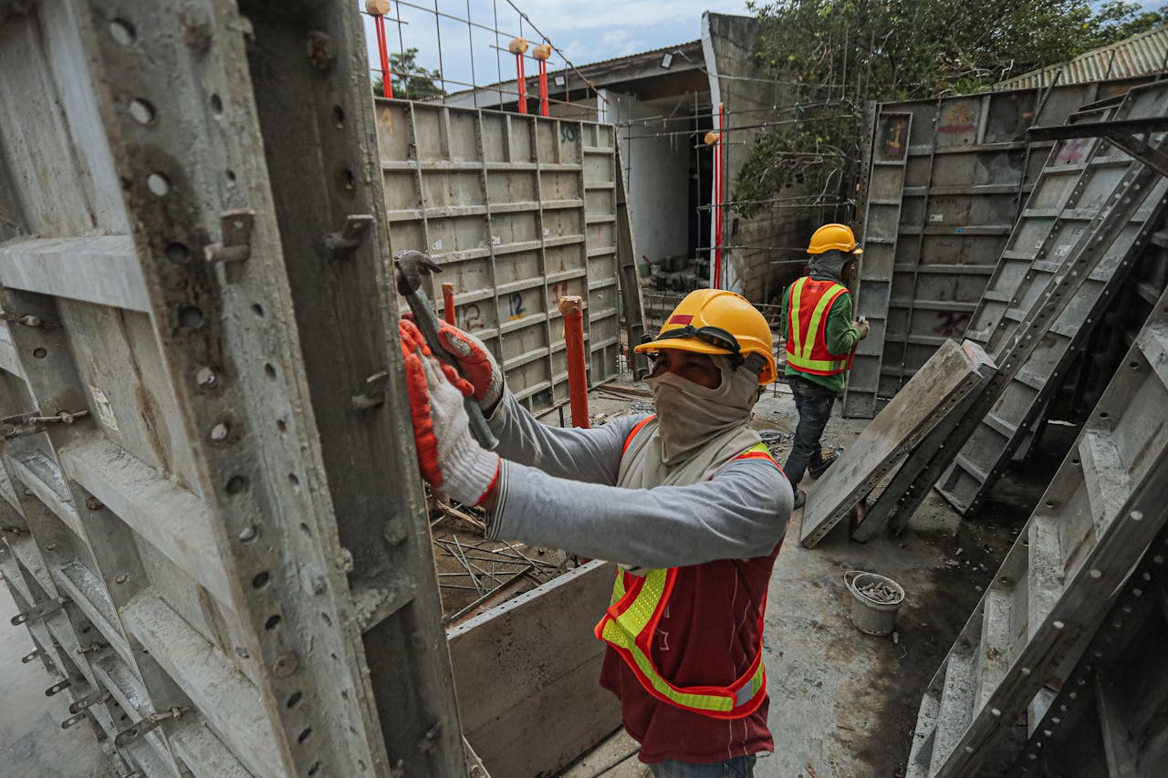 Construction workers in helmets and safety gear working on an outdoor building site.